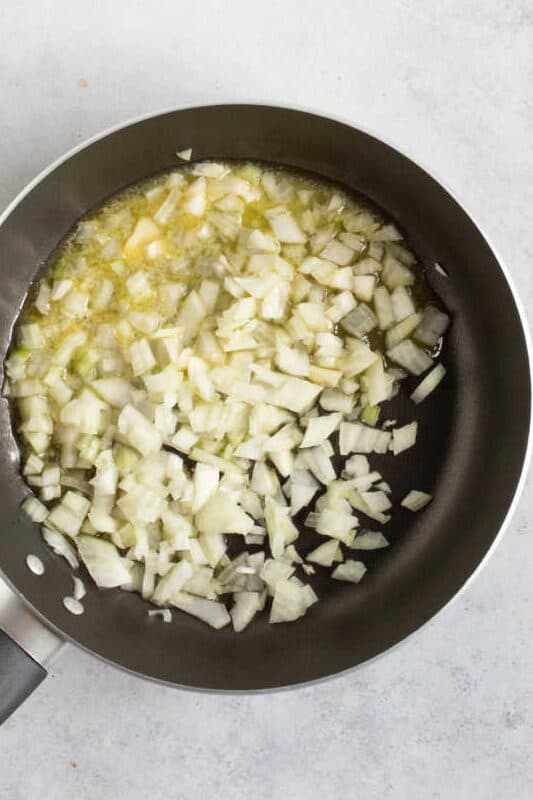 Onions frying in butter in a black frying pan.