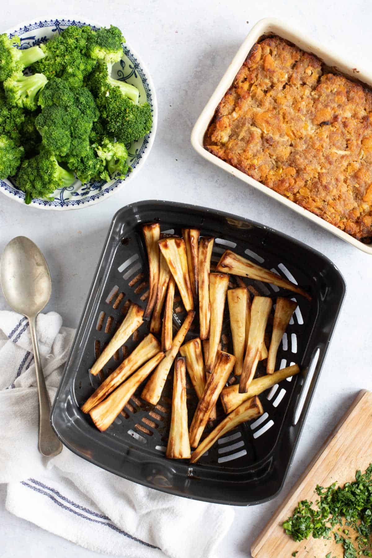 Roast parsnips in air fryer basket with broccoli and stuffing on the side.