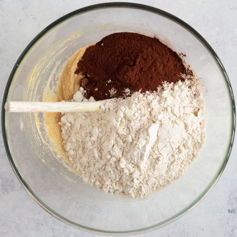 Plain flour and cocoa added to cookie dough in bowl.