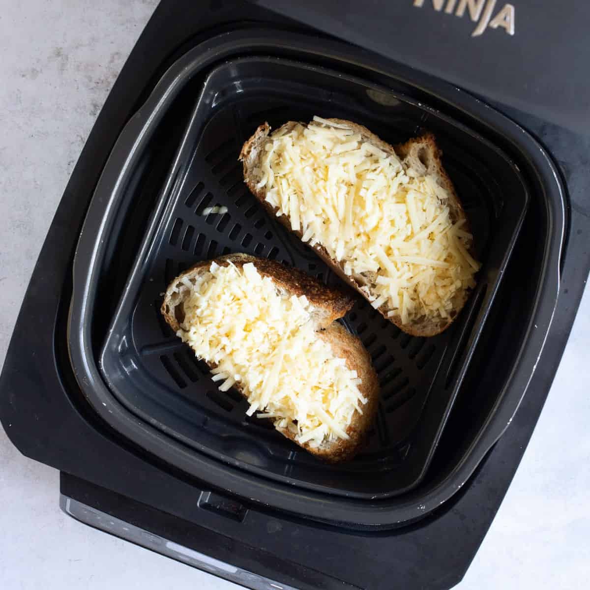 Two slices of cheese on toast in Ninja air fryer.