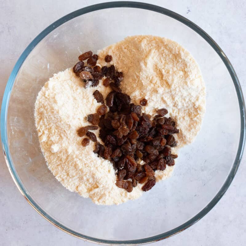 Flour, butter, sugar and dried fruit in a bowl.