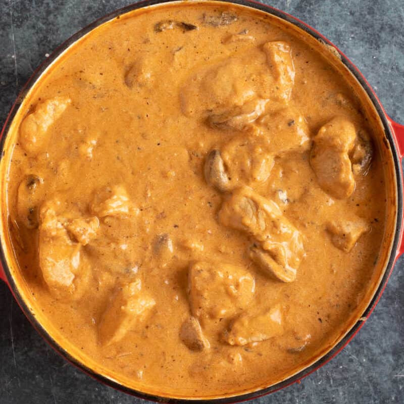 Creamy pork and mushroom stroganoff in a red pan.