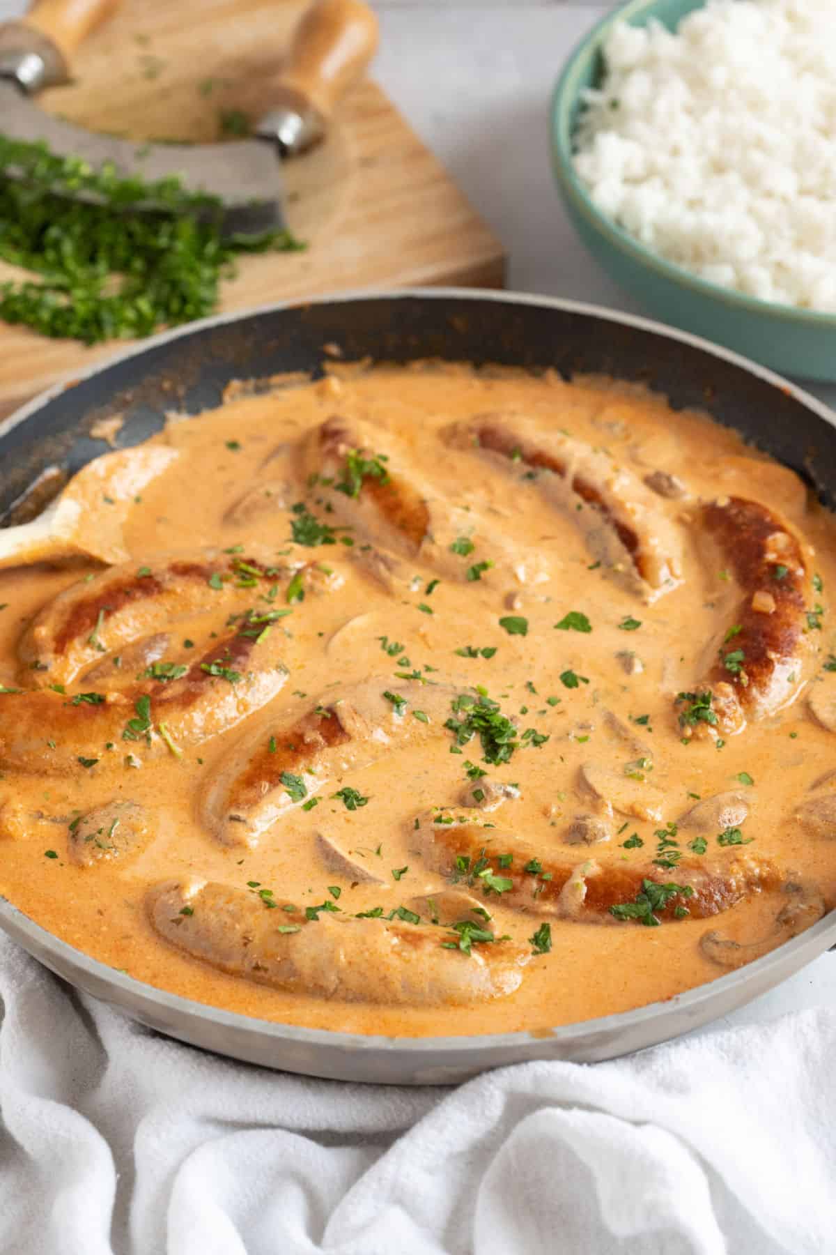 A pan of sausage stroganoff with a bowl of rice.