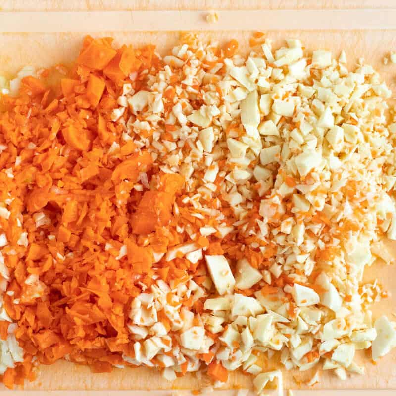 Chopped up onion, carrots and parsnips on a board.