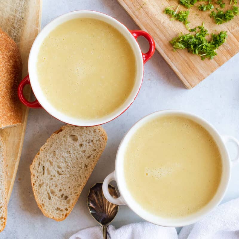 Two bowls of leek and potato soup with bread.