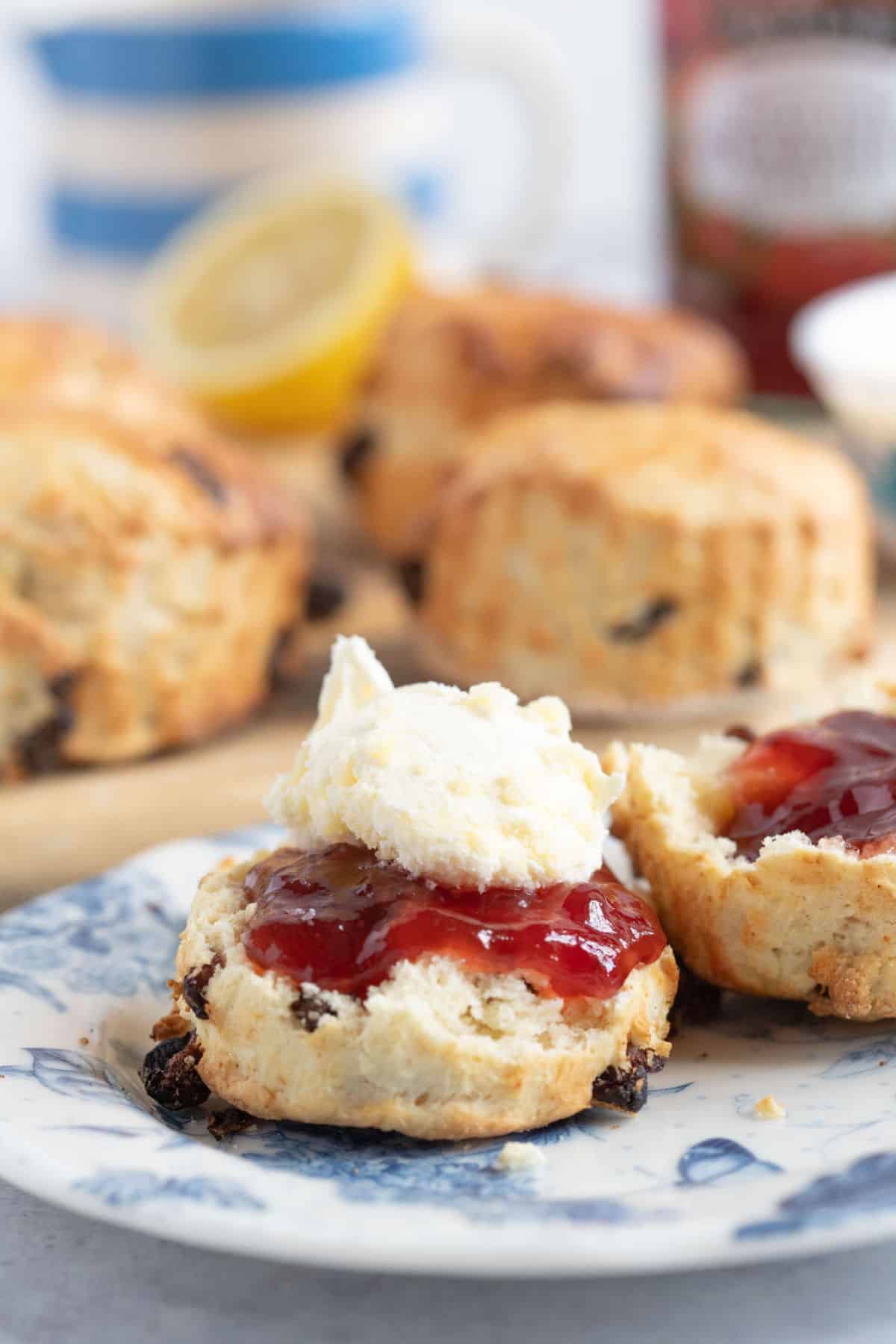 A fruit scone on a blue and white plate topped with jam and clotted cream.