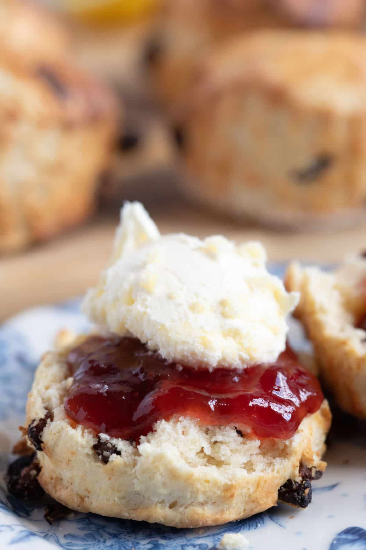 Half a fruit scone spread with jam and clotted cream.