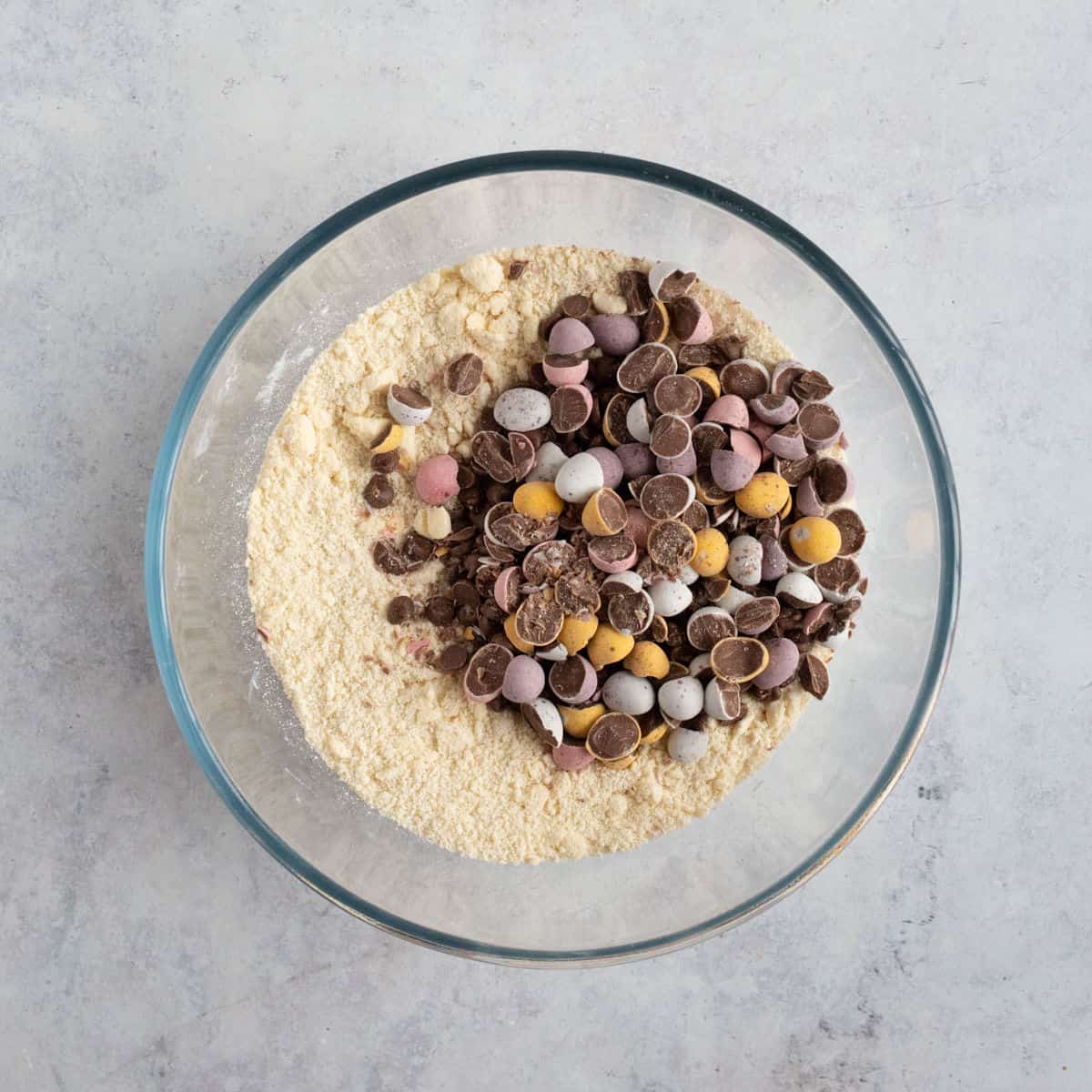 Chopped mini eggs added to shortbread dough in a bowl.