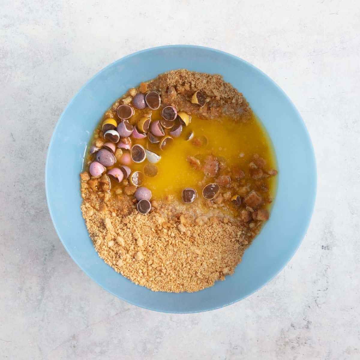A bowl with crushed digestives, melted butter and mini eggs.