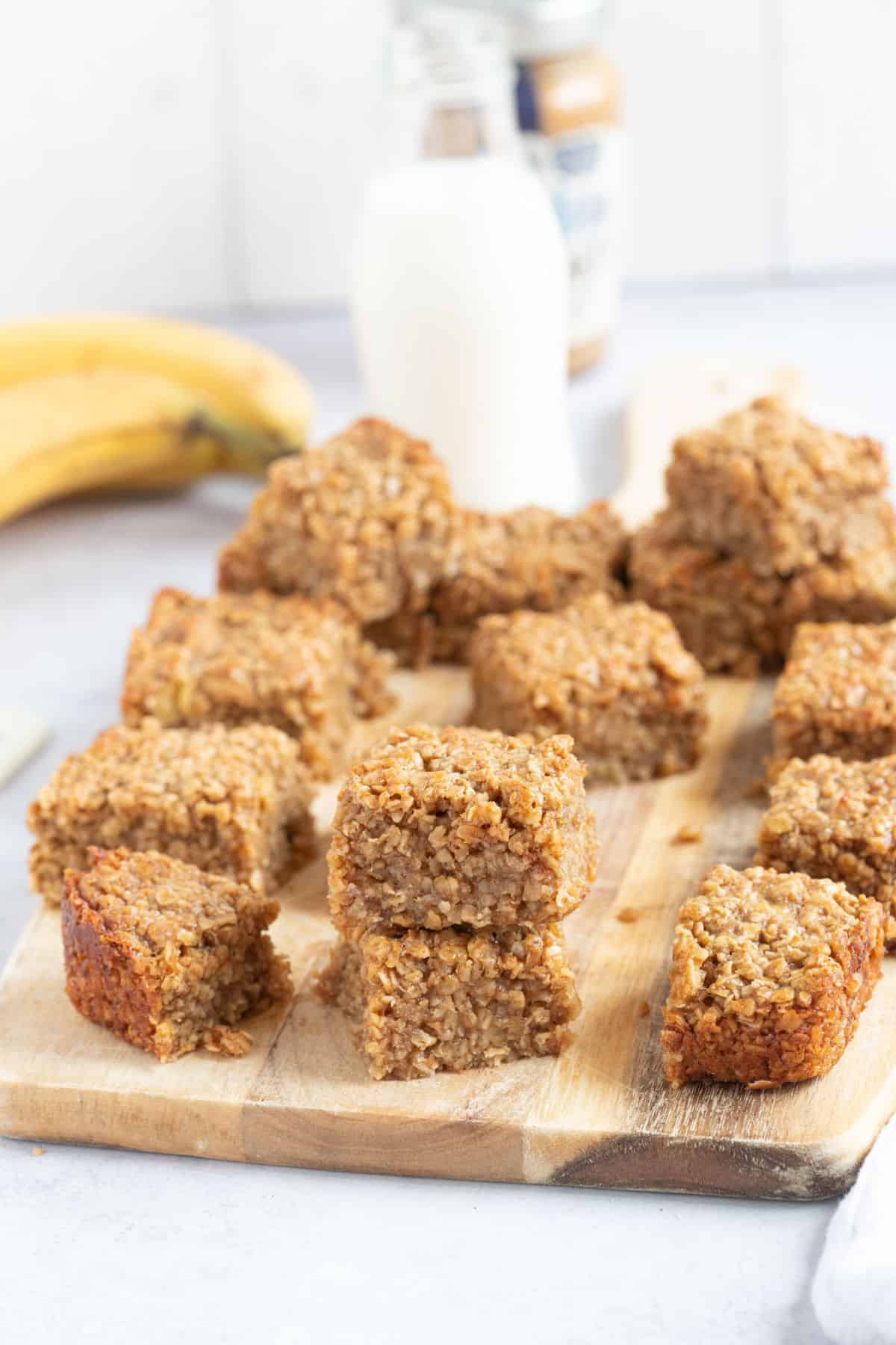 Banana peanut butter and honey flapjack bars on a wooden board with a glass of milk.
