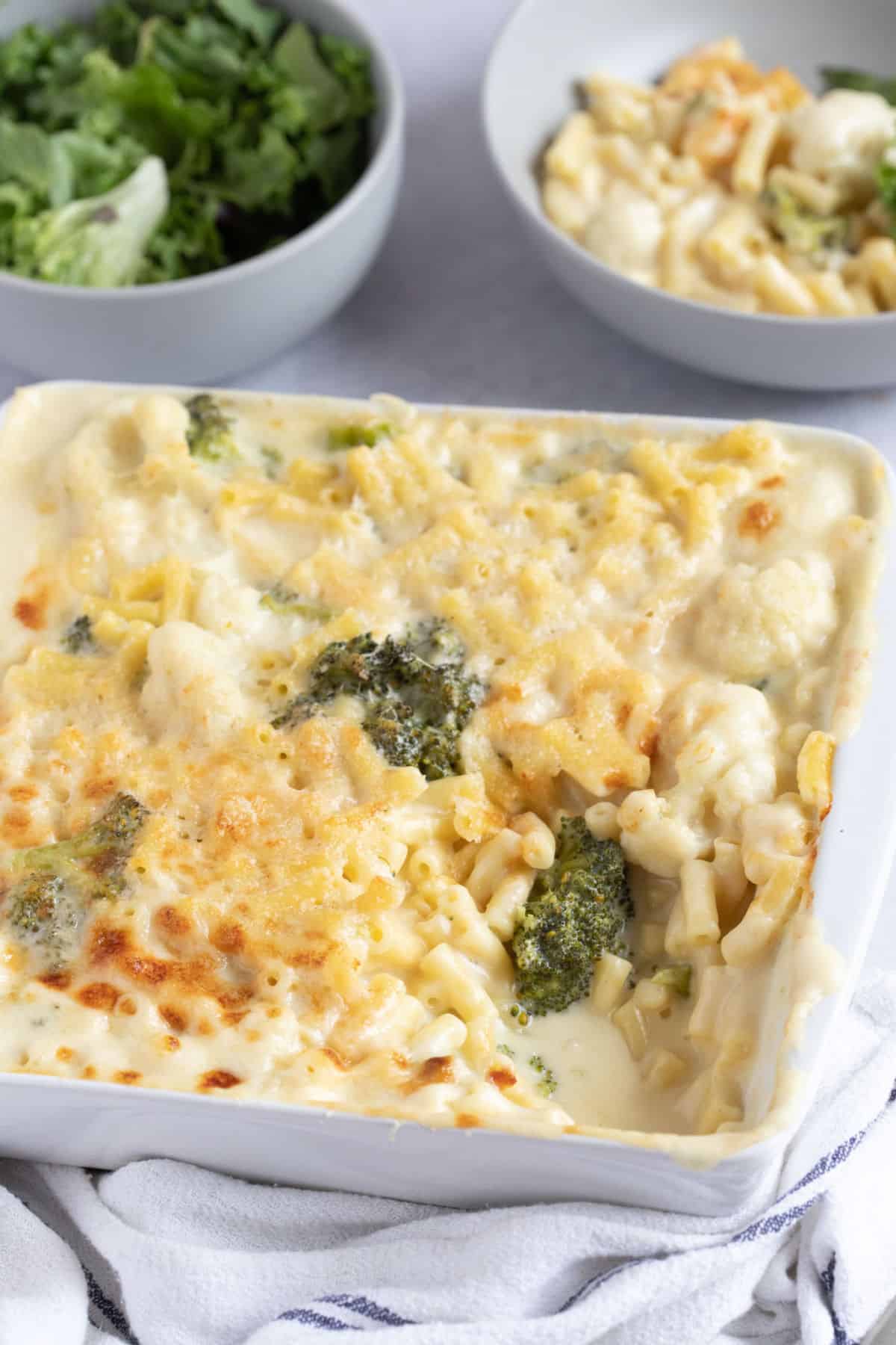 Broccoli and cauliflower macaroni cheese in a baking dish with a bowl of salad behind.