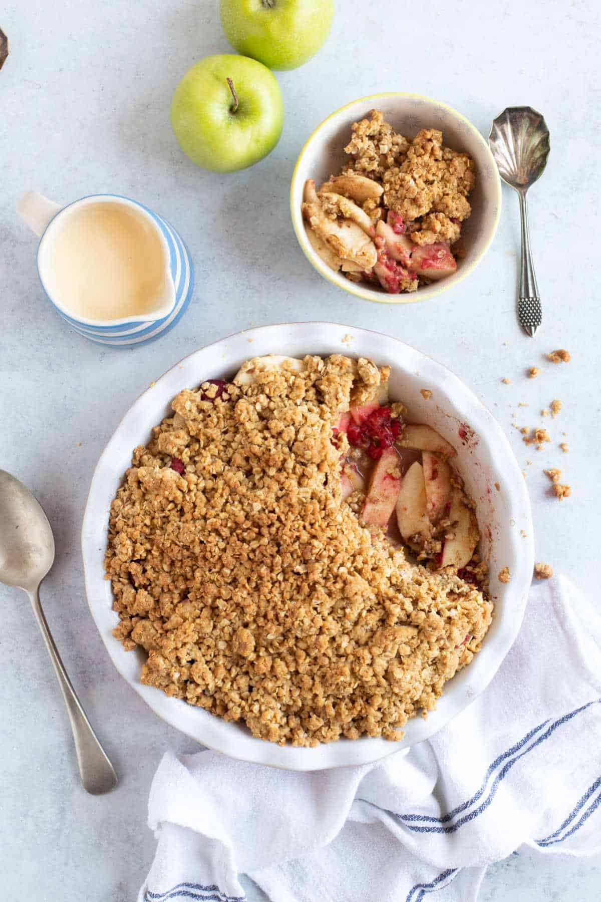 Apple and raspberry crumble in a serving dish with a jug of custard