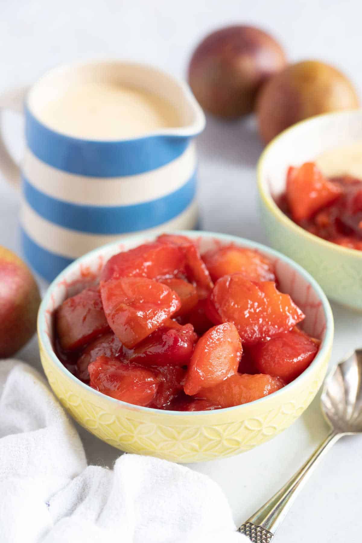 Plum compote in a bowl with a jug of custard in background.