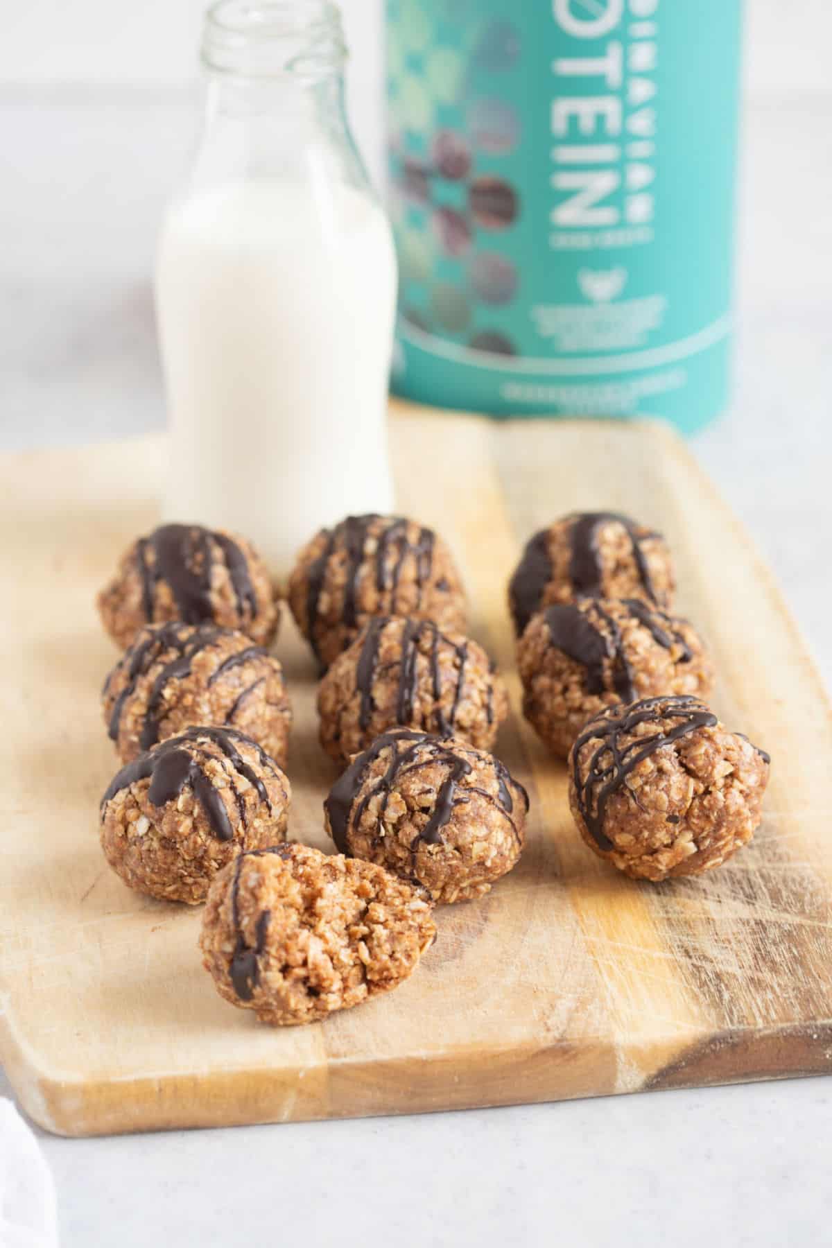 Half eaten vanilla protein ball in front of a line of protein balls on wooden board.