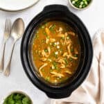 Slow cooker chinese chicken curry in a slow cooker basin, with plates to the side.