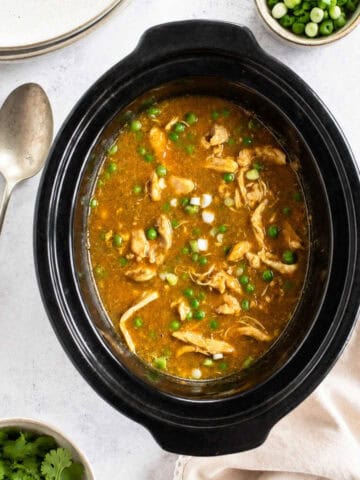 Slow cooker chinese chicken curry in a slow cooker basin, with plates to the side.