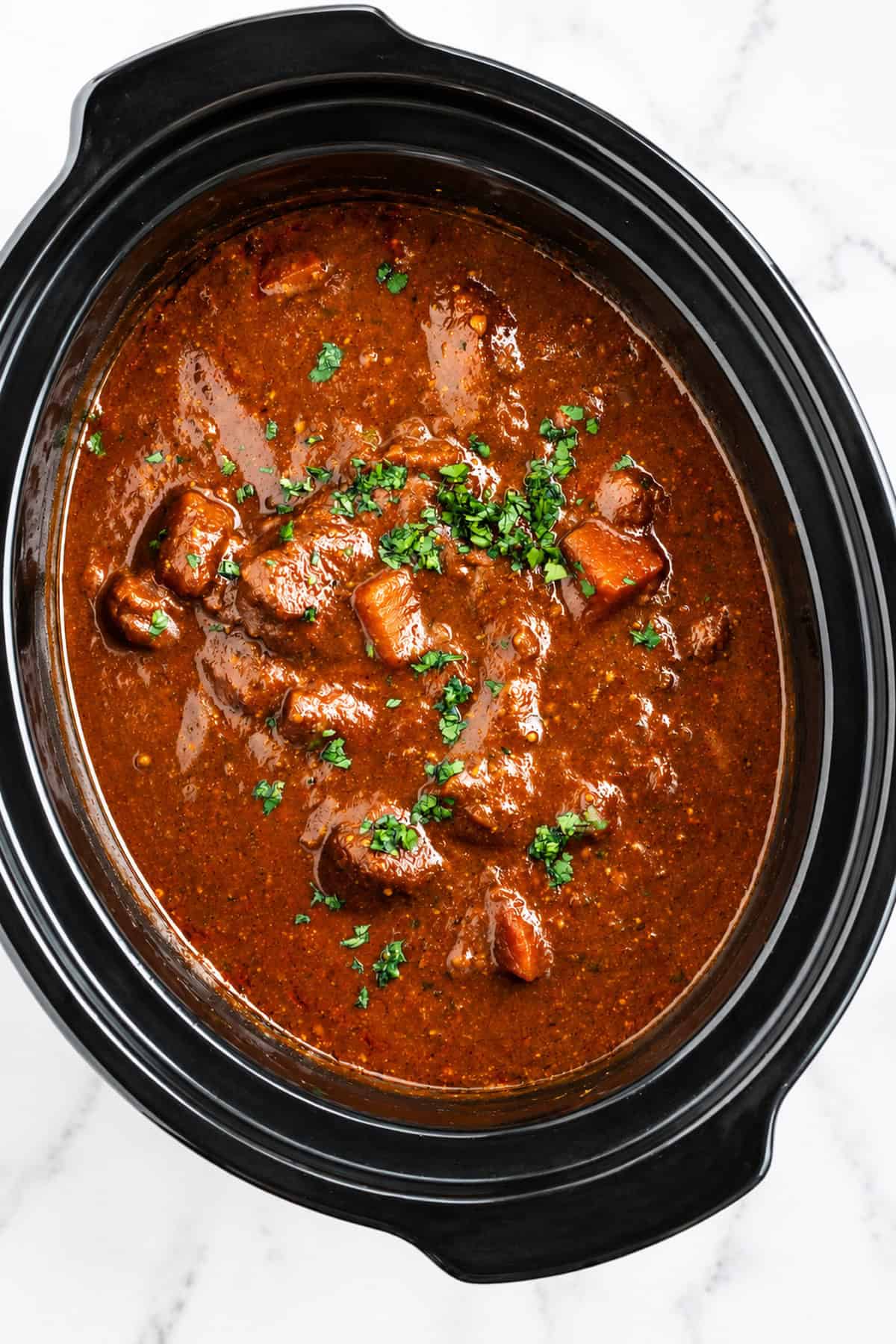 Slow cooker lamb curry in black slow cooker basin with freshly chopped coriander sprinkled on it.