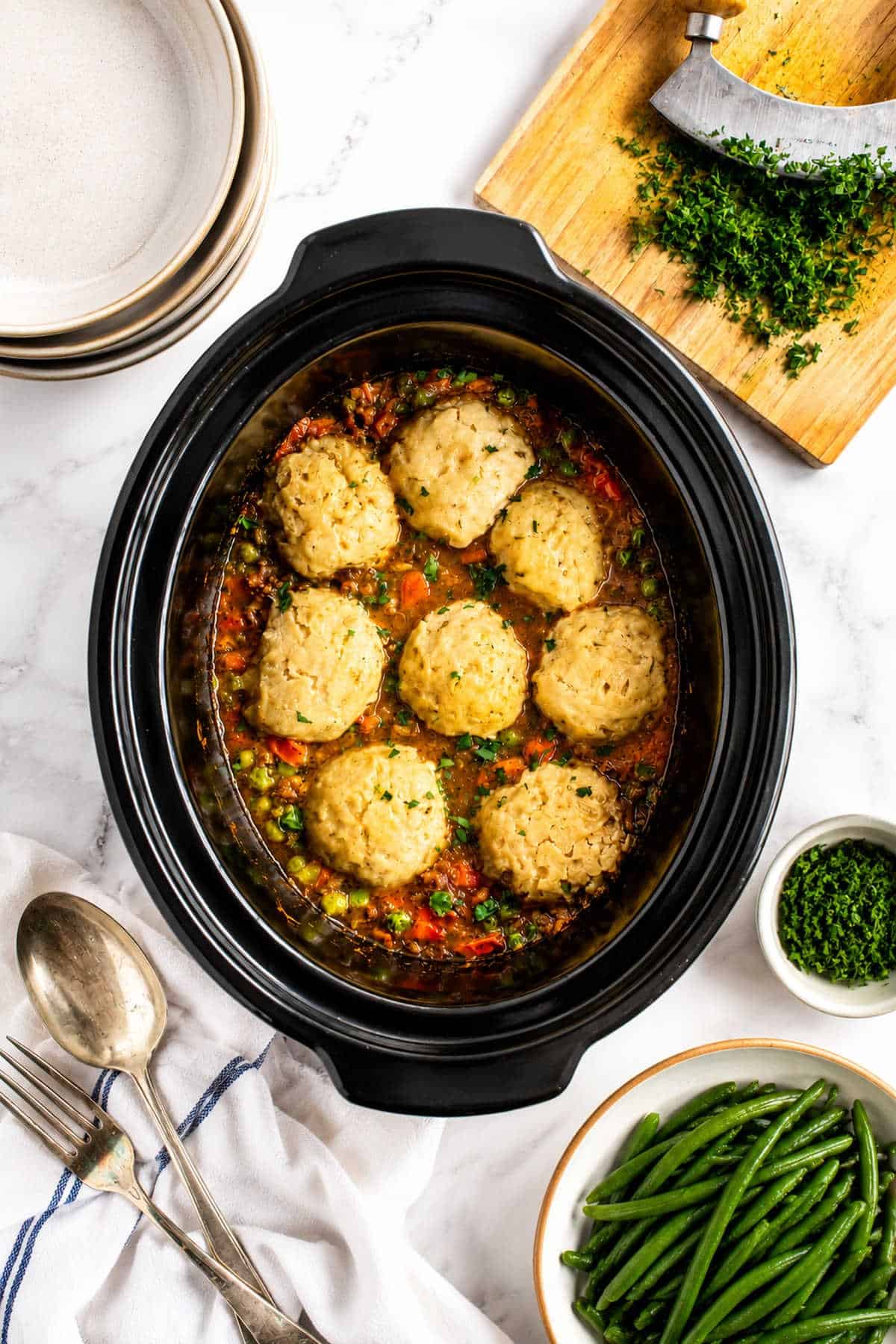 Slow cooker mince and dumplings in black slow cooker basin with a side of green beans.