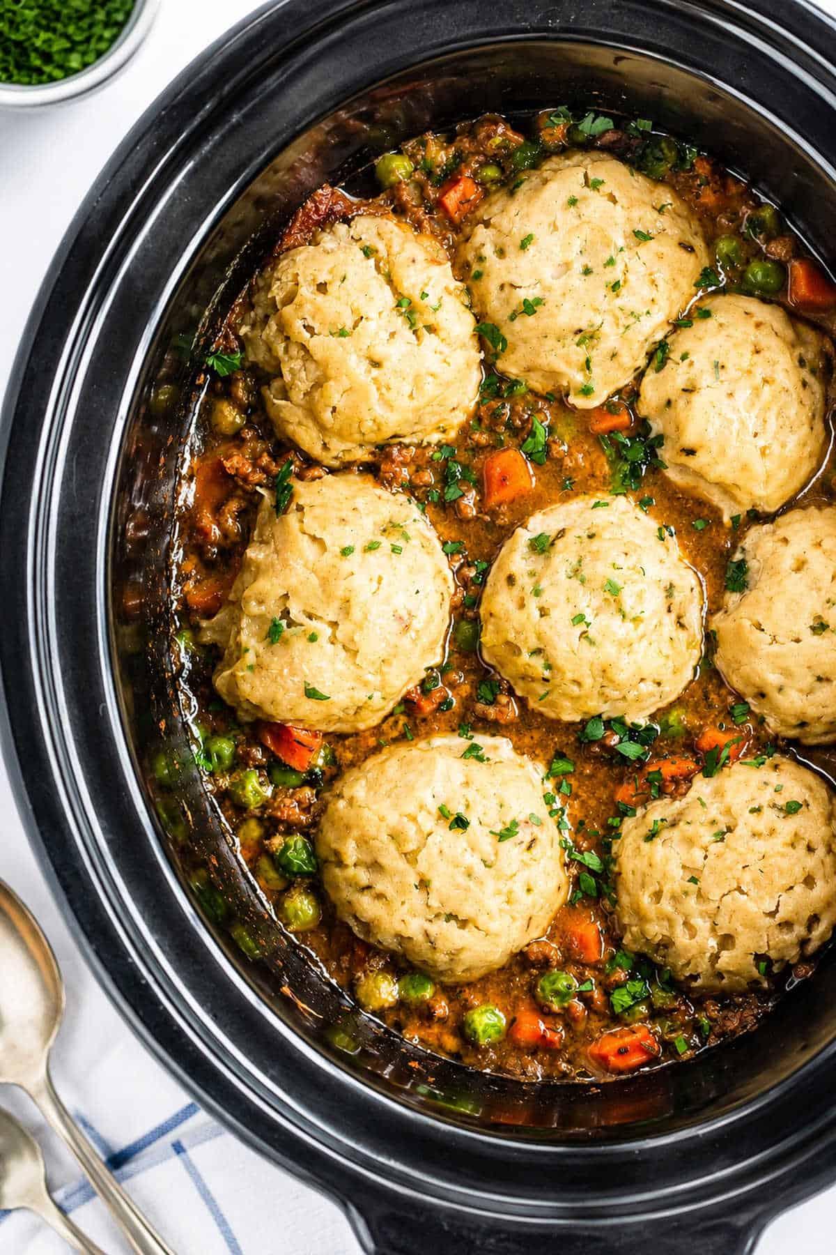 Slow cooker mince and dumplings in slow cooker with parsley garnish.