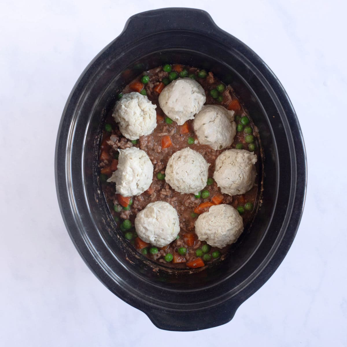 Uncooked suet dumplings on top of the slow cooker mince in slow cooker.