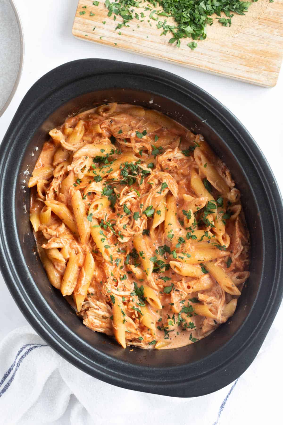 Slow cooker chicken pasta in a slow cooker basin sprinkled with parsley.
