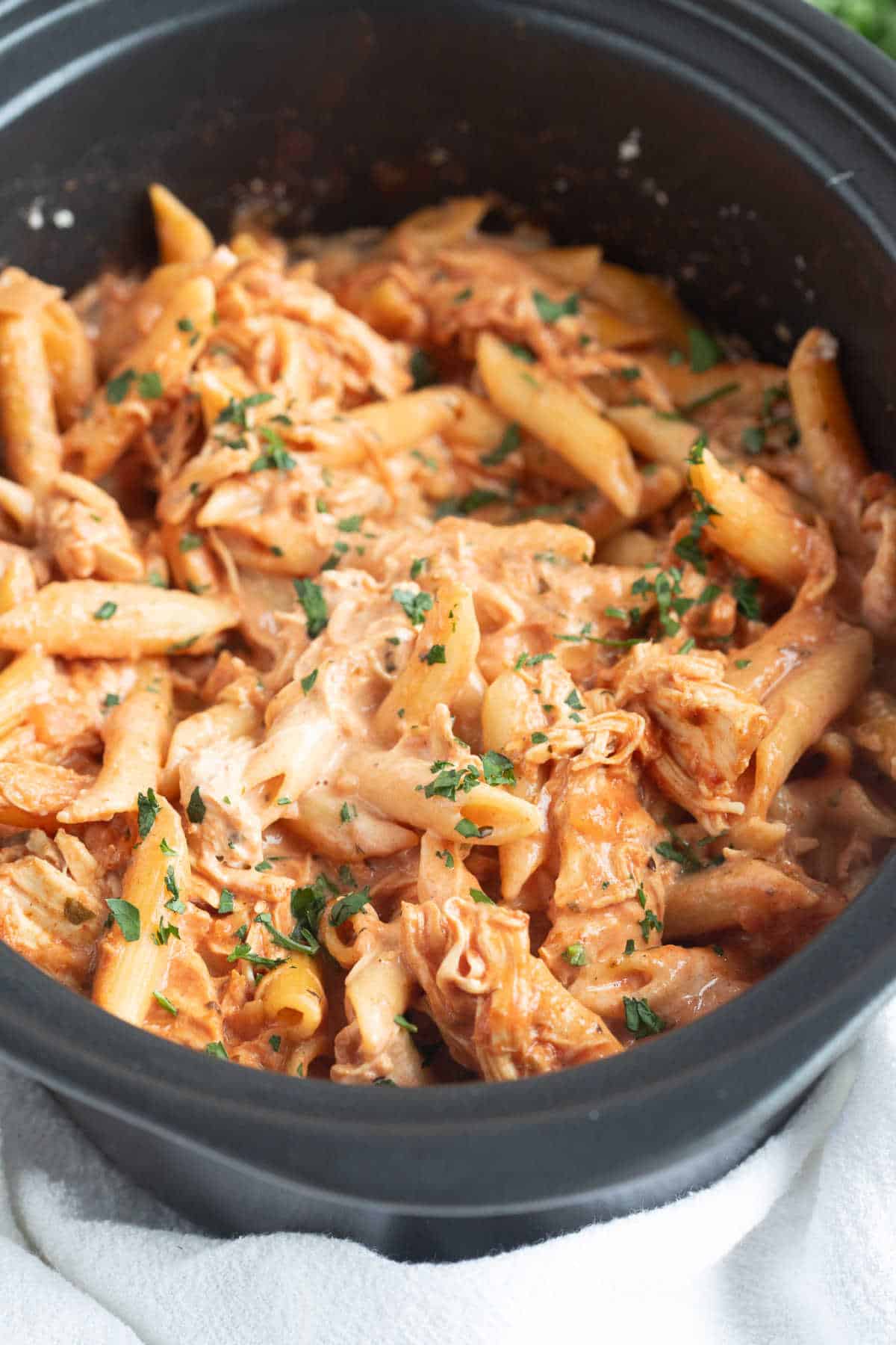 A close up of creamy crockpot chicken pasta in a slow cooker.