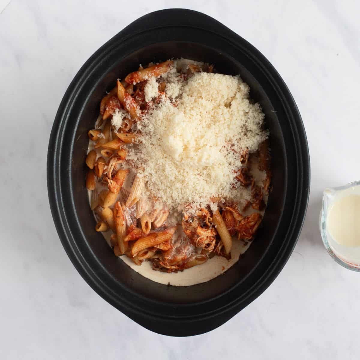 Adding cream and Parmesan to the slow cooker chicken pasta.